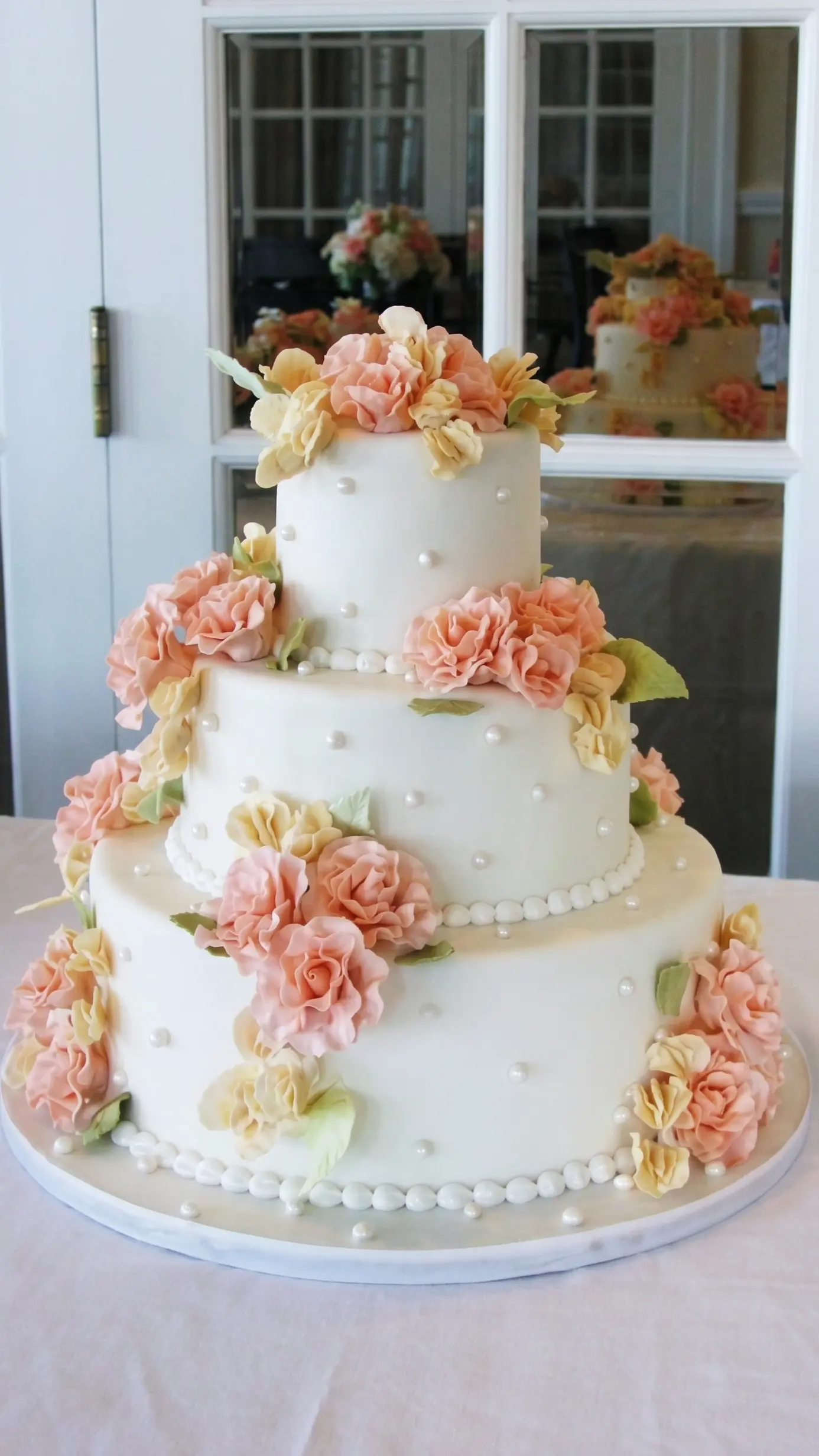 Three-tier white wedding cake decorated with peach and cream sugar flowers and pearl details